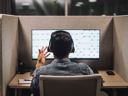 Rear view of young male customer service executive talking through headset sitting at desk in illuminated call center