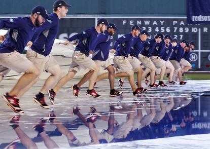 Un grupo de voluntarios se apresuran a extender una lona en el campo de juego durante una tormenta en el partido en Boston entre los Boston Red Sox y los Minnesota Twins.