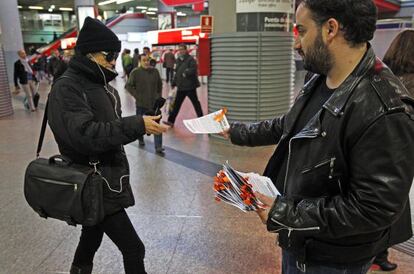 Uno de los voluntarios de la Oficina Precaria entrega folletos con lazos naranjas en Atocha.