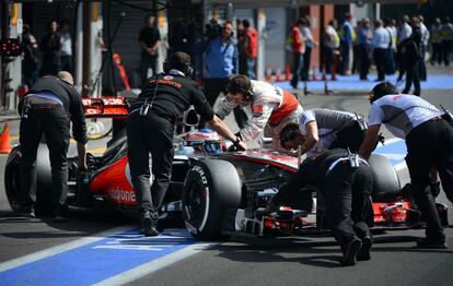 Los mecánicos de McLaren introducen el coche de Jenson Button en boxes.