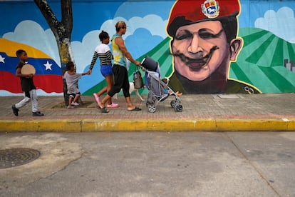 Una familia camina frente a un mural con el rostro del expresidente Hugo Chávez, este lunes en Caracas