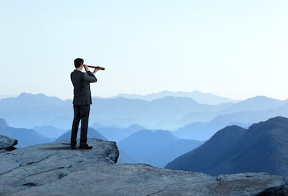 Businessman With Spyglass Looking Out Toward Mountain Range