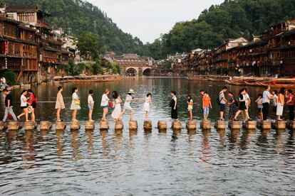 This photo taken on August 5, 2017 shows visitors walking on stone piers crossing the Tuojiang River in the ancient town of Fenghuang in Xiangxi, in China's central Hunan province.
The old town district of Fenghuang nestles on the banks of a winding river in a picturesque, mountainous part of Hunan province, and boasts stunning Qing and Ming dynasty architecture dating back hundreds of years. / AFP PHOTO / STR / China OUT