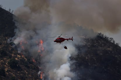 El principal incendio forestal en la capital se registra en Curacaví, al nororiente, donde el fuego ya ha afectado más de 2.000 hectáreas y se acerca a sectores poblados e infraestructura crítica. De esas llamas, propiciadas por las altas temperaturas y la baja humedad, proviene la gran masa de humo tóxico que nubla el cielo santiagueño. En la imagen, bomberos a bordo de un helicóptero intentan sofocar un incendio en Curacavi, el 15 de diciembre de 2022.