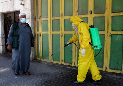 Un trabajador del departamento de salud del municipio palestino de Hebrón, vestido con un EPI (equipo de protección personal), desinfecta una calle de la ciudad.
