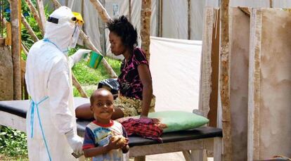 Un sanitario ofrece agua a una enferma de &eacute;bola en presencia de un ni&ntilde;o en un centro de aislamiento de Kenema (Sierra Leona.