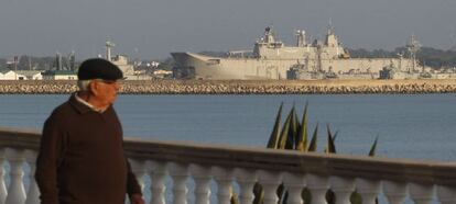 Un hombre pasea por el paseo marítimo de Rota. Al fondo, la base naval.