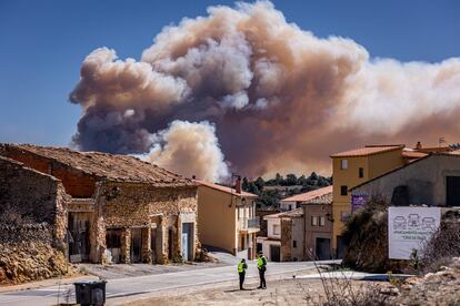 Una pareja de guardias civiles impide al acceso a Villanueva de Viver, municipio donde se originó el incendio el pasado jueves. En la imagen, tomada sobre las 13 horas del lunes, se ve la enorme nube de humo provocada por el rebrote del fuego en las inmediaciones de Montán.