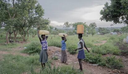 Tres mujeres llevan bidones llenos de agua desde un pozo hasta sus hogares en el campo de refugiados Rhino Camp, en Uganda.