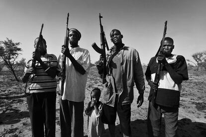 Sudan del Sur. Un grupo de pastores dinkas alza sus AK-47 al aire en las cercanías de Dubek, en Warrap. Décadas de guerra han sumido al país en una violencia arraigada en los hombres desde que nacen hasta que mueren. Los Dinka son la etnia dominante en Sudan del Sur con casi el 70% de la población total, unos 3 millones de personas. El actual presidente, Salva Kir, pertenece a este grupo étnico. En su sociedad todo gira en torno al ganado, pero las hambrunas les afectan igual puesto que raramente se alimentan de él. Suelen ir armados para protegerlo de ataques y robos. La leche debería ser una fuente de nutrientes, pero la falta de pastos frescos en la dieta de los animales hace que dicho líquido sea poco nutritivo.