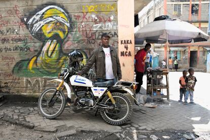 Tyrese posa junto a su moto a las afueras del centro de juventud. A su lado se asoma Wambua, que asoma desde su puesto de comida en el que vende chapatti. Cuatro de cada diez jóvenes desempleados en los slums monta su propio negocio y los quioscos de comida son la opción más popular. 