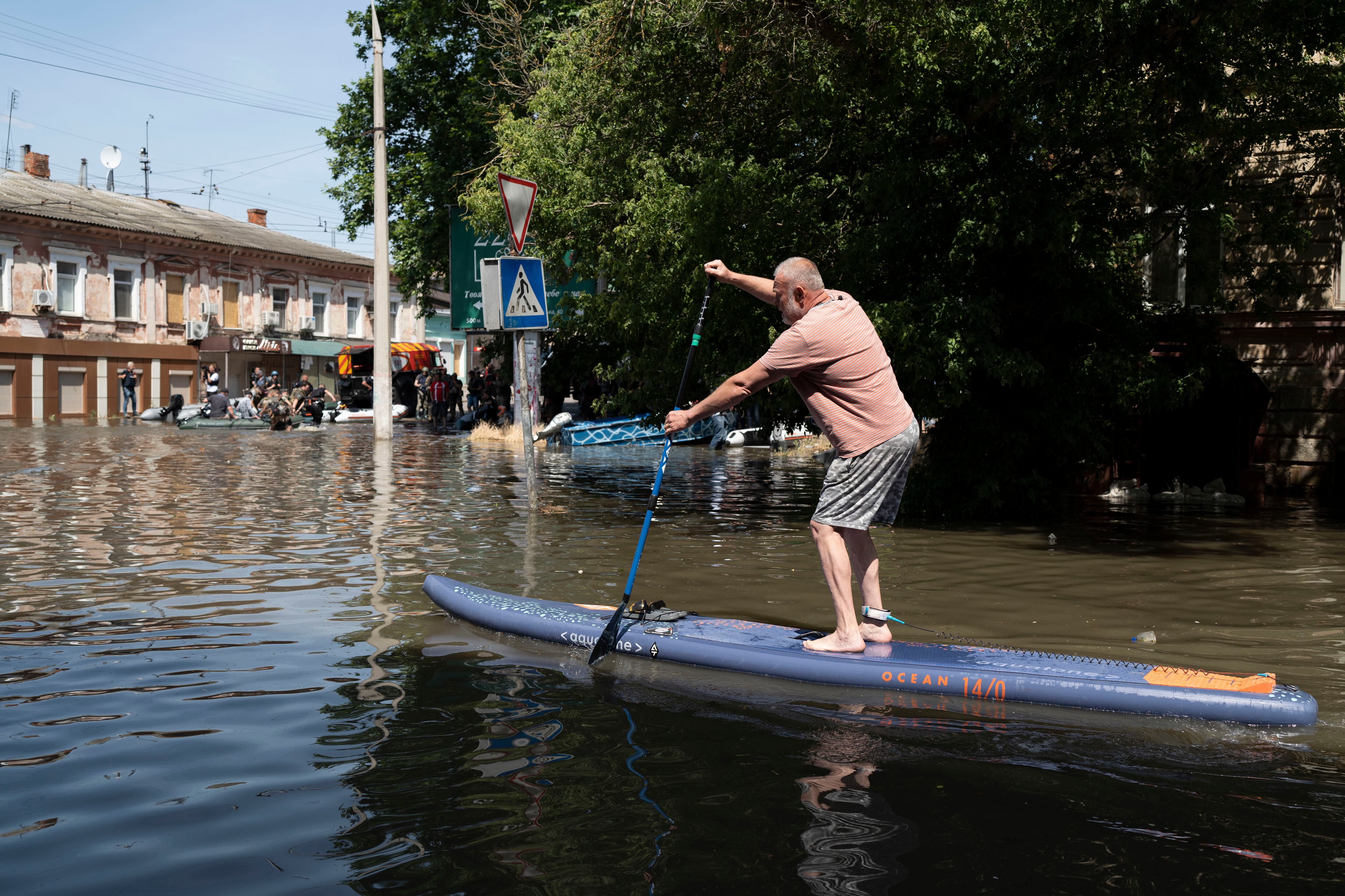 Un hombre utiliza una tabla de paddle surf para moverse por una calle inundada en Jersón. 