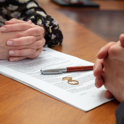 Signing a divorce, marriage dissolution documents and agreement. Wife and husband hands, wedding rings and legal papers for signature on a wooden table, lawyer office