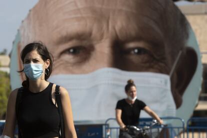 Dos mujeres pasan frente a una cartel que anima a la ciudadanía a usar mascarillas en Tel Aviv. Israel aprobó, este jueves, endurecer el confinamiento el viernes, una semana después de imponerlo, dejando la actividad económica en el mínimo esencial y limitando rezos y manifestaciones.