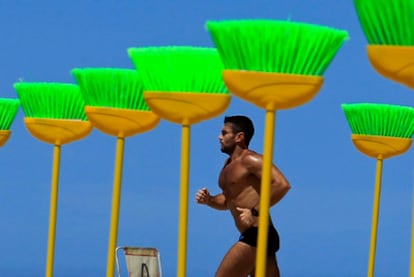 Un hombre corre entre las escobas verdes en la playa de Copacabana.