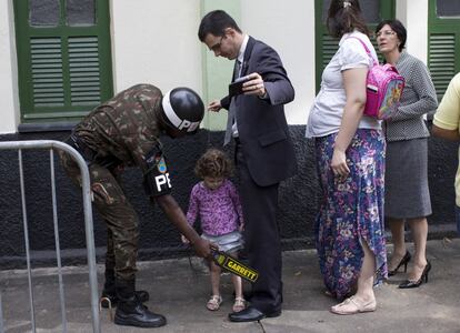 Un soldado brasileño registra a un hombre junto a su hija, en el exterior de un centro electoral de Río de Janeiro.