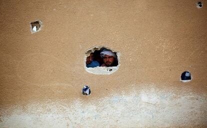 TOPSHOT - Displaced Syrians, who fled the countryside surrounding the Islamic State (IS) group stronghold of Raqa, look through a hole in a wall at a temporary camp in the village of Ain Issa on April 28, 2017. / AFP PHOTO / DELIL SOULEIMAN