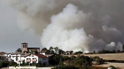 Columna de humo, tras unas casas, en el incendio forestal declarado en un monte cercano a la localidad de Sorauren (Navarra).