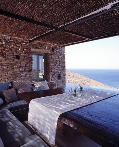 Cubierto por una pérgola de cañizo, el porche de la casa vuelca sus vistas sobre el Egeo y aprovecha los muros de piedra para convertirlos en bancos corridos. Los almohadones son de la empresa especializada en tejidos resistentes al sol y al salitre Sunbrella, y la mesa de madera es un diseño de la propia interiorista griega Marilena Rizou.