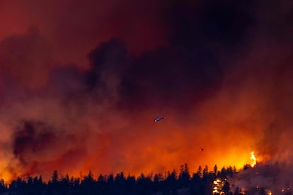 A helicopter battles the McDougall Creek wildfire as it burns in the hills West Kelowna, British Columbia, Canada, on August 17, 2023, as seen from Kelowna.