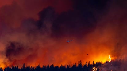 A helicopter battles the McDougall Creek wildfire as it burns in the hills West Kelowna, British Columbia, Canada, on August 17, 2023, as seen from Kelowna.