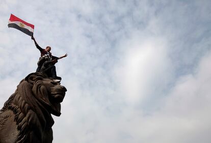 Un manifestante, encaramado a una estatua, hondea una bandera egipcia en El Cairo.