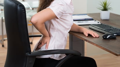 Una chica tocándose la espalda baja sentada en una silla de oficina.