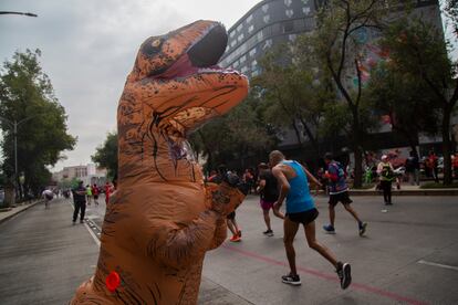 Una mujer disfrazada de dinosaurio anima a los corredores que participan en el Maratón de la Ciudad de México 2022.