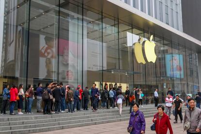 Una fila de clientes guarda turno frente a una tienda de Apple.