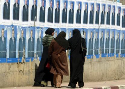 Tres mujeres argelinas pasean junto a un muro lleno de carteles electorales en Argel.