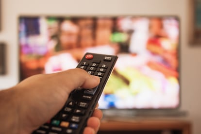 Una persona sostiene un mando a distancia ante el televisor.