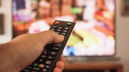 Una persona sostiene un mando a distancia ante el televisor.