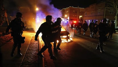 Policías antidisturbios pasan ante un coche en llamas durante las protestas que se han producido en la madrugada de este martes en Ferguson.