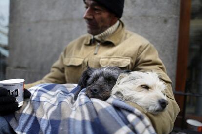 Un hombre con sus dos perros pide en una calle de Madrid.