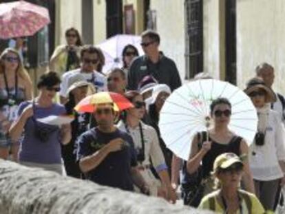 Turistas se protegen del sol con sombrillas y diferentes sombreros durante su paso por la Carrera del Darro en Granada.