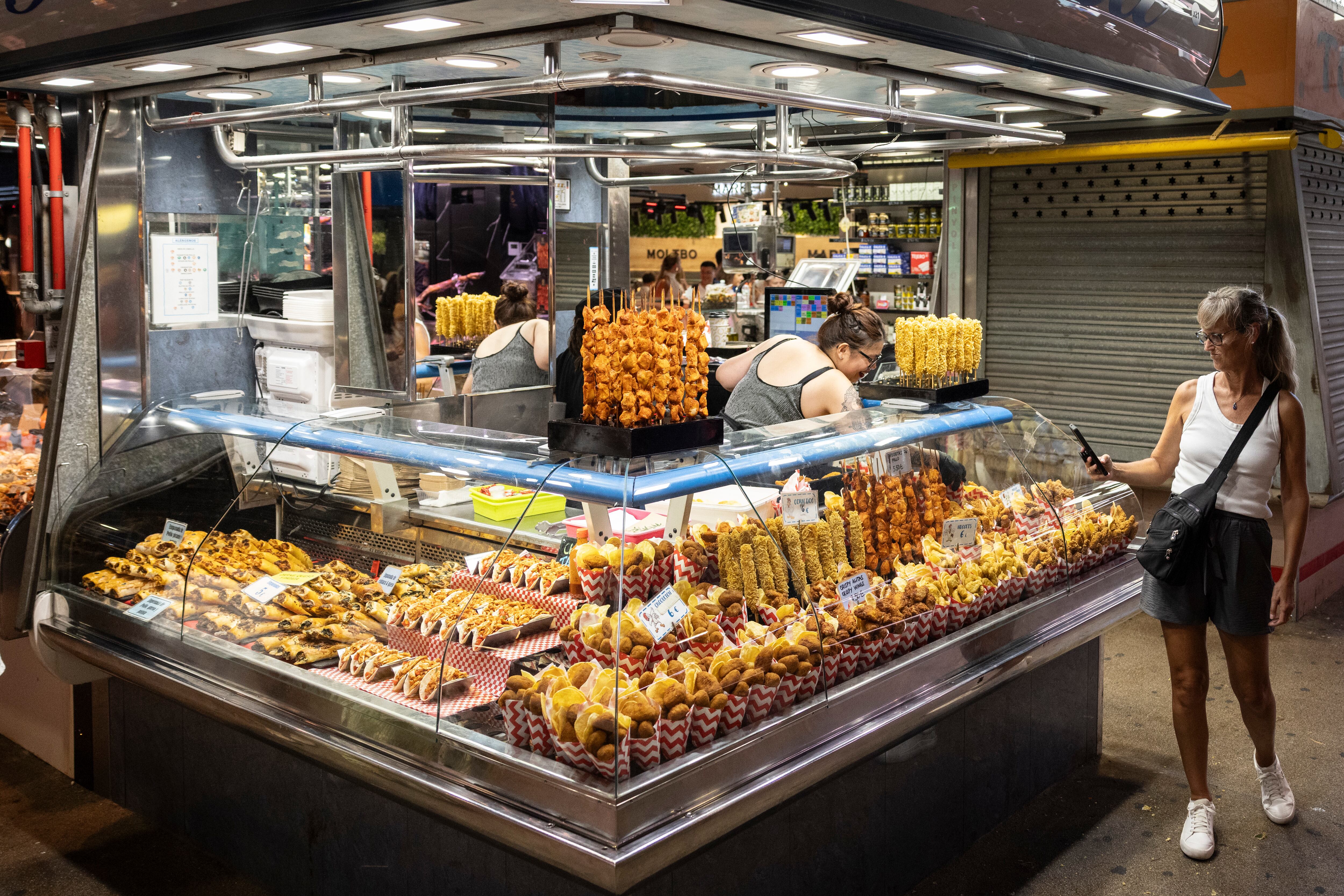 Una turista fotografia los cuchuruchos y pinchos de comida preparada para llevar en el mercado de La Boqueria de Barcelona, este jueves.