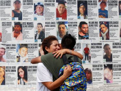 Una mujer abraza a su hijo frente a un mural con información de personas desaparecidas en México