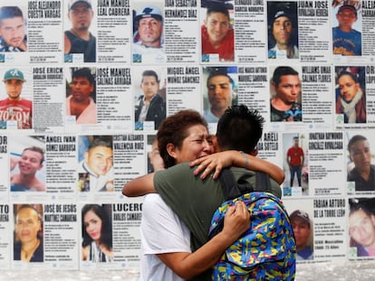 Una mujer abraza a su hijo frente a un mural con información de personas desaparecidas en México