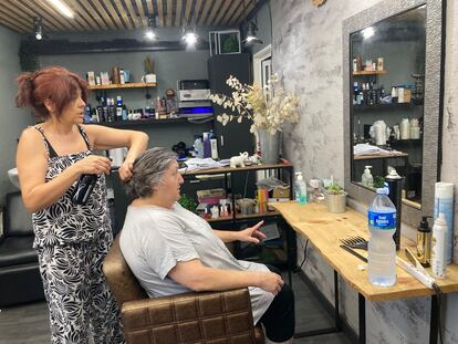 Mari Carmen Bermúdez humedece el pelo con un dosificador a una clienta de su peluquería.
