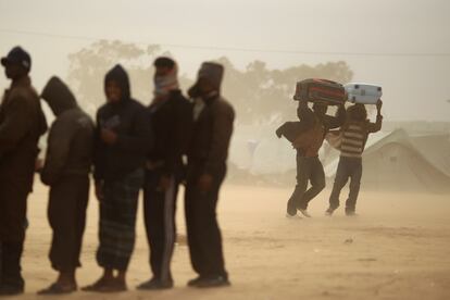 Dos hombres caminan entre la tormenta de arena, mientras otros hacen cola para obtener alimentos en el campo de refugiados de Ras Jdir, en Túnez.