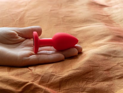 Red silicone smooth anal plug, sex toy, on an orange background in a girl's hand. Contrast photo of anal toys, erotic toys