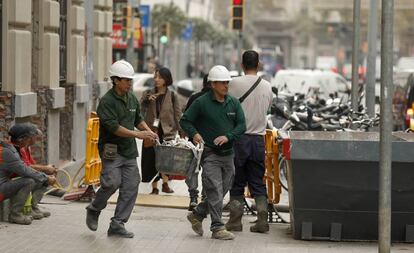 Dos trabajadores de la empresa Construcciones Peña Mateos echan escombros en un contenedor en una calle de Barcelona.