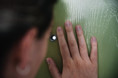 Una mujer observa el rellano de su edificio a través de la mirilla de su puerta.