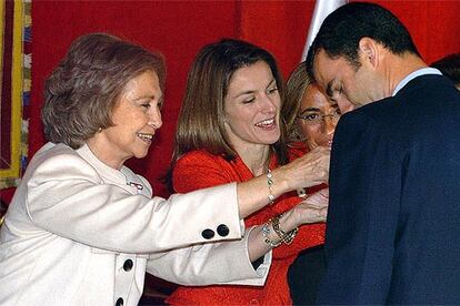 Doña Sofía y doña Letizia colocan una banderita cada una en la solapa del príncipe, tras depositar su donativo en la mesa instalada cerca del Congreso.