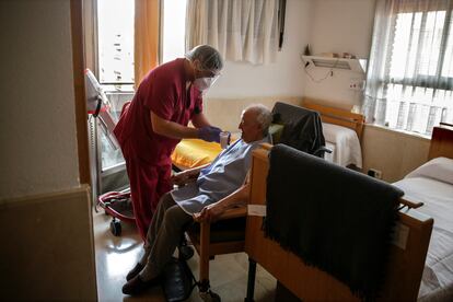 Un empleado le da líquido a un hombre mayor en una de las habitaciones en una Residencia de ancianos en Madrid