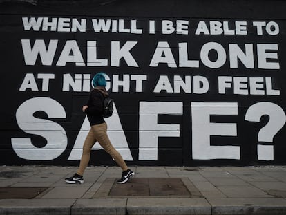 Una joven camina junto al último mural de la artista irlandesa Emmalene en el centro de Dublín en marzo de 2021. La inscripción dice: "¿Cuándo podré caminar sola por la noche y sentirme segura?".