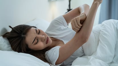 Una chica rascándose el brazo en la cama.