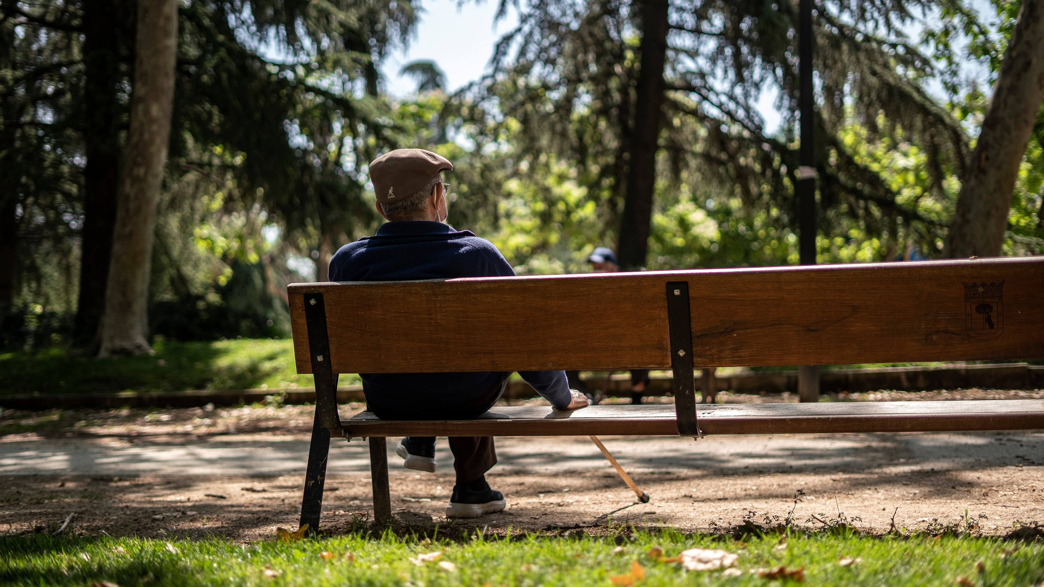 Un hombre mayor sentado en un banco de un parque de Madrid.

