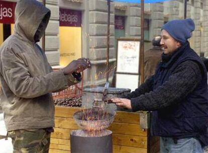 Dos vendedores ambulantes se calientan las manos ante un tradicional asador de castañas ubicado en una céntrica calle de Granada.