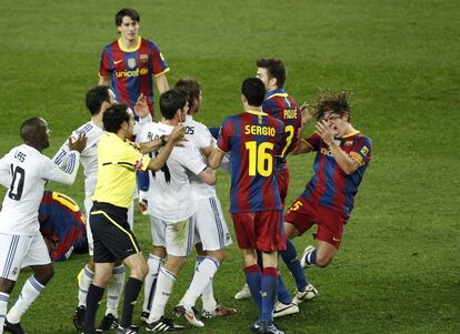 Iturralde González (2º izqda.) muestra la tarjeta roja al defensa del Real Madrid Sergio Ramos mientras el capitán del FC Barcelona, Carles Puyol (drcha.) cae empujado durante el partido Liga ante el FC Barcelona disputado el 29 de noviembre de 2010 en el Nou Camp (Barcelona).